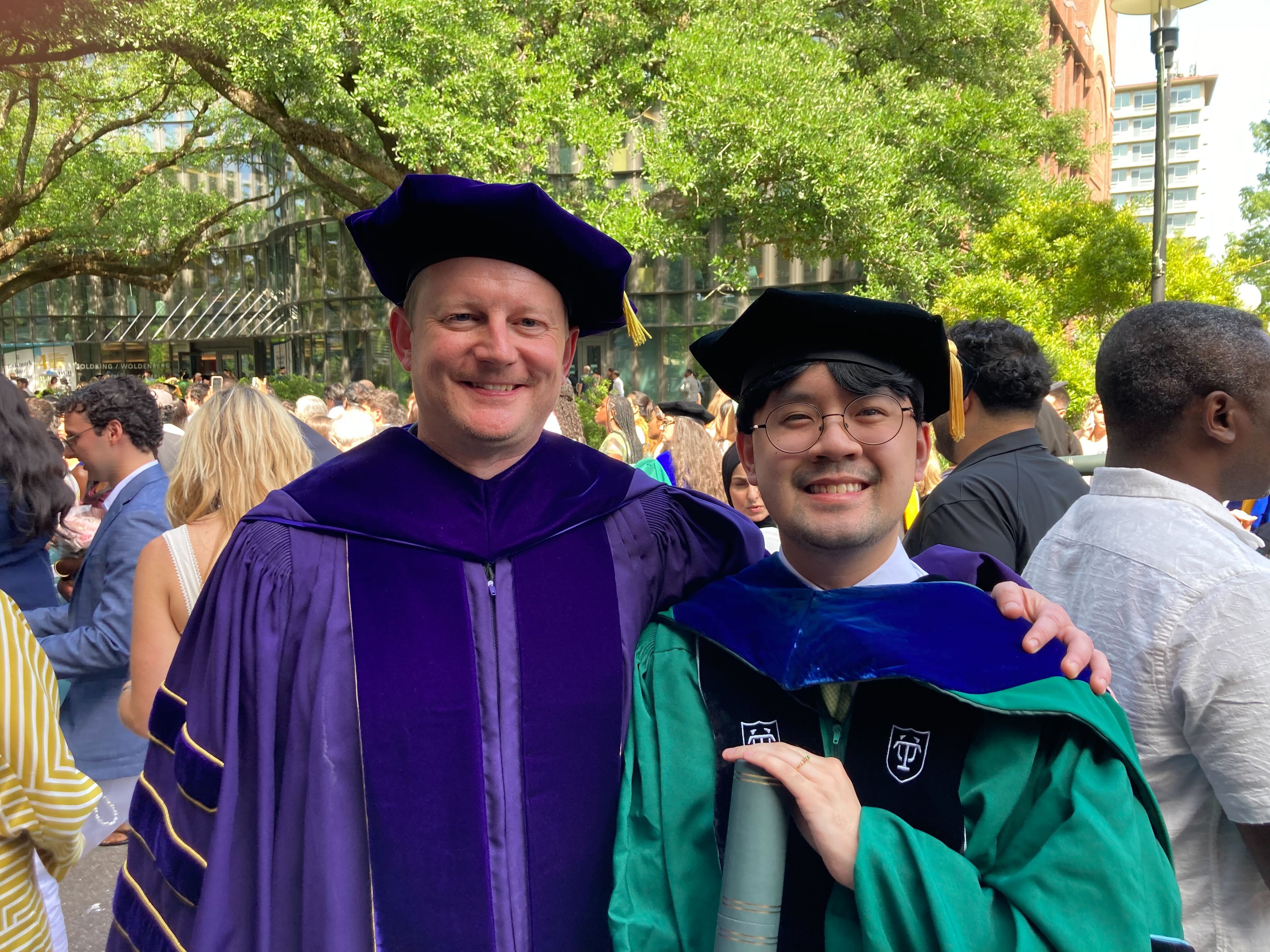Dr. Le standing next with Dr. Fadok in their commencement attire