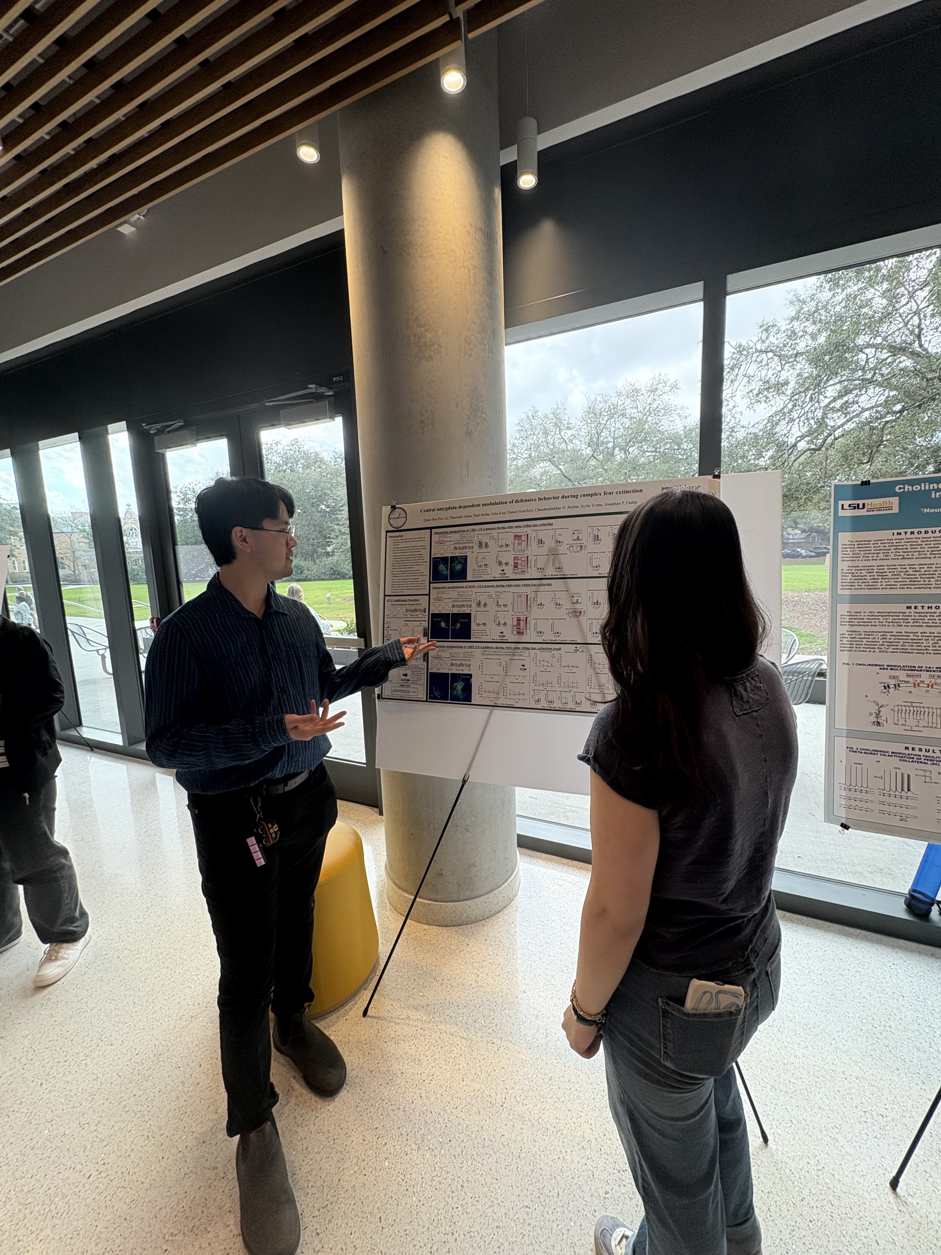 Eric is standing next to his poster presenting to a student.