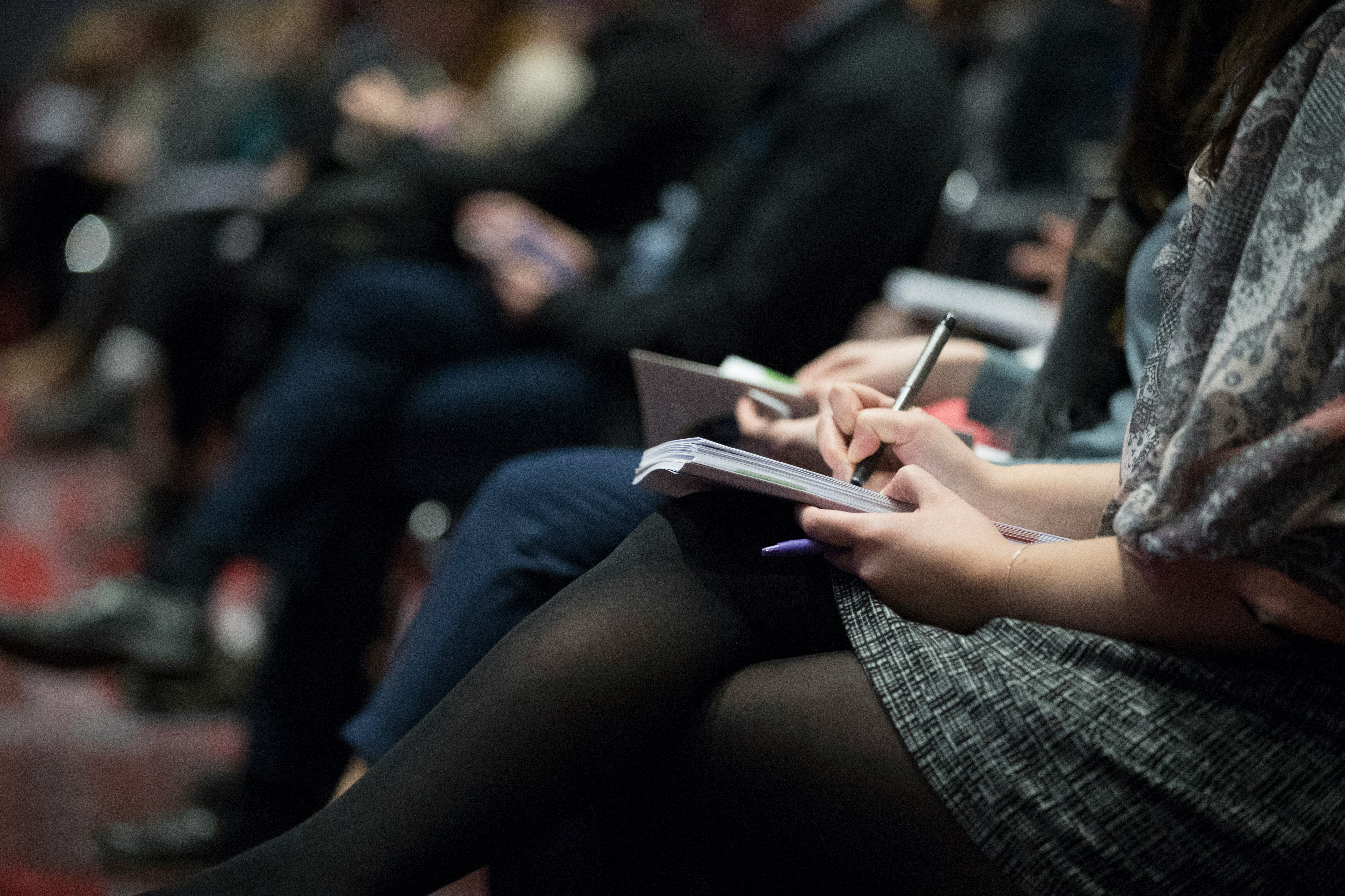 People in an auditorium taking notes in a notebook.
