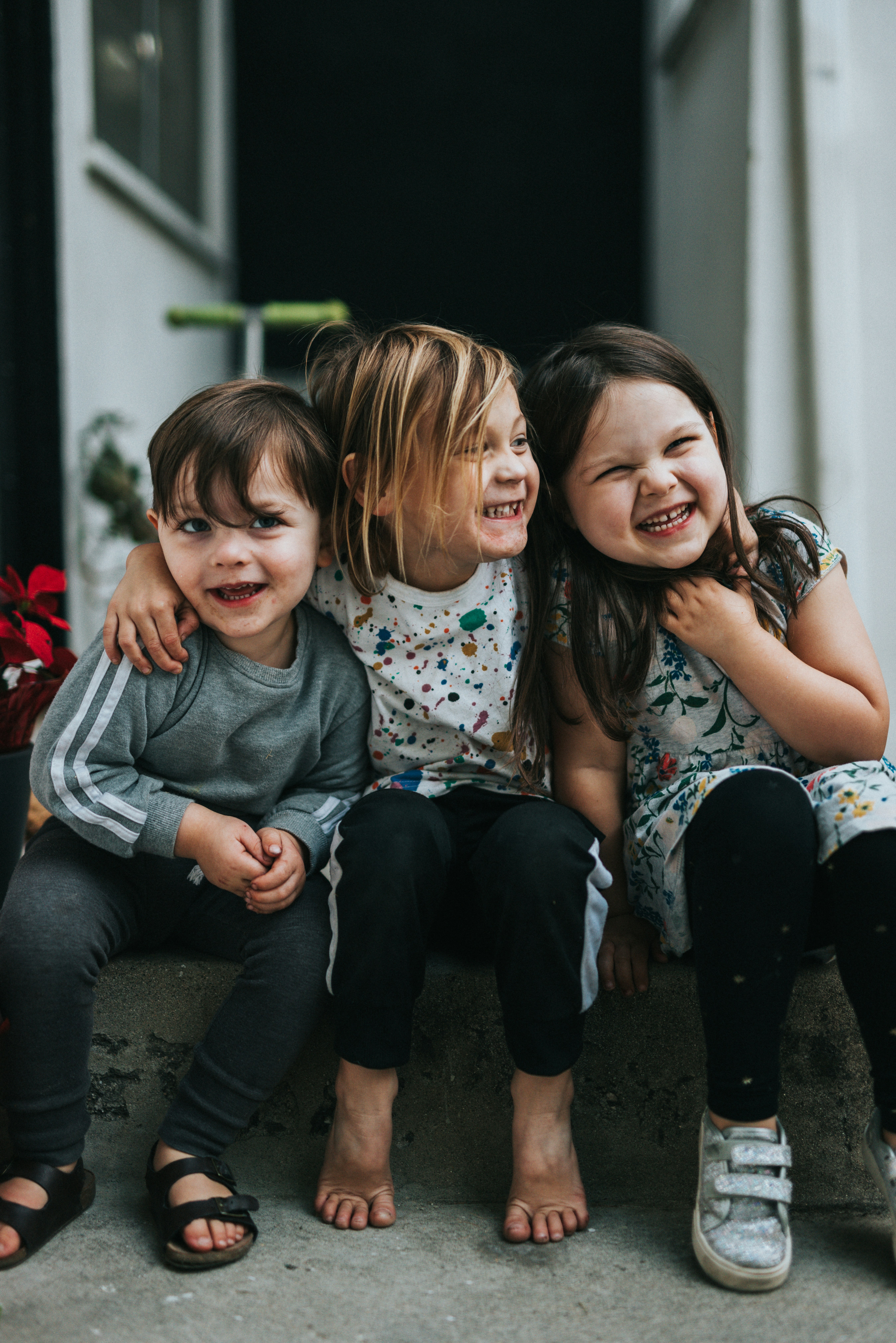 Three children, two girls and a boy, sit on a concrete step and smile.