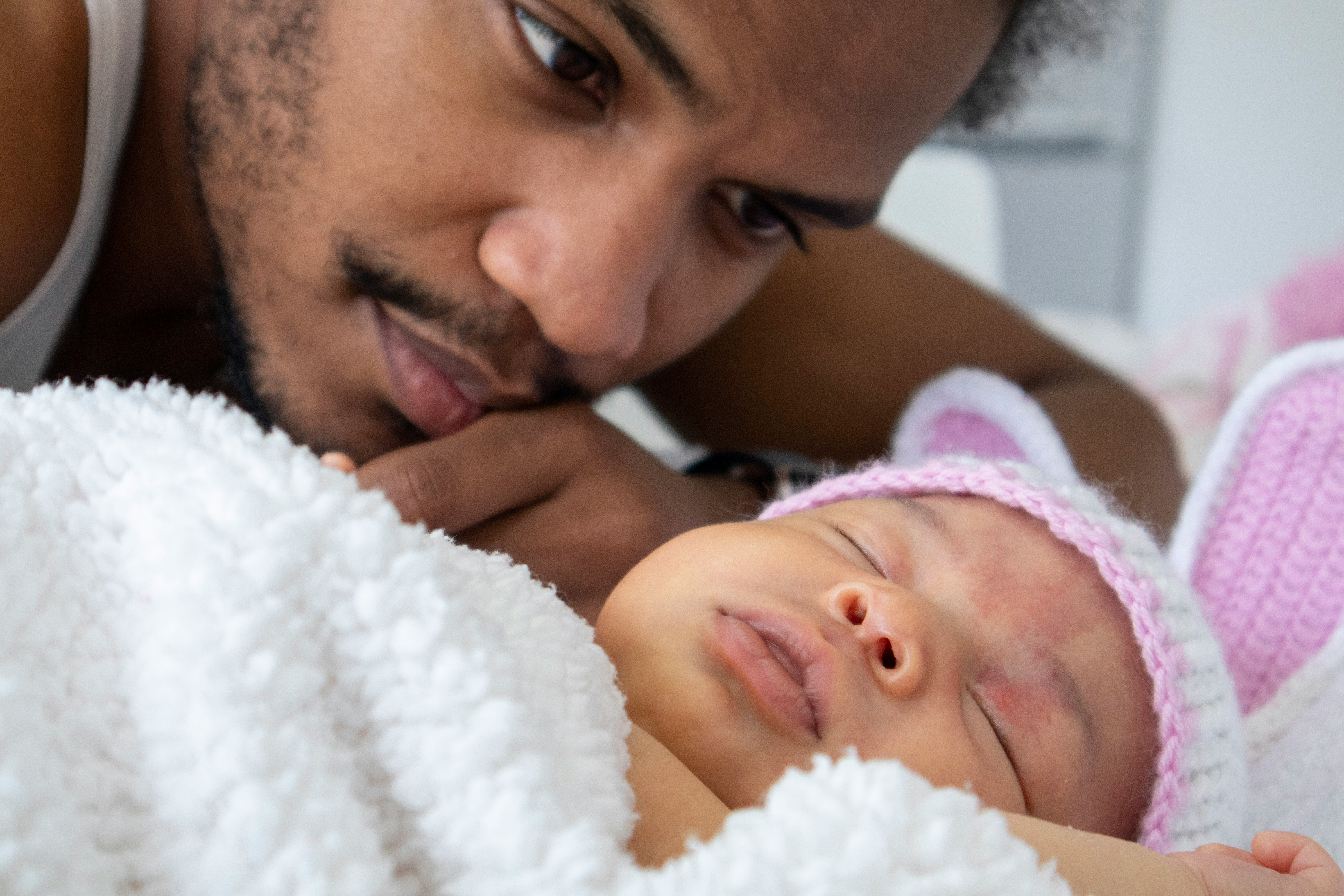 A father looking down at his sleeping baby with a pink hat.