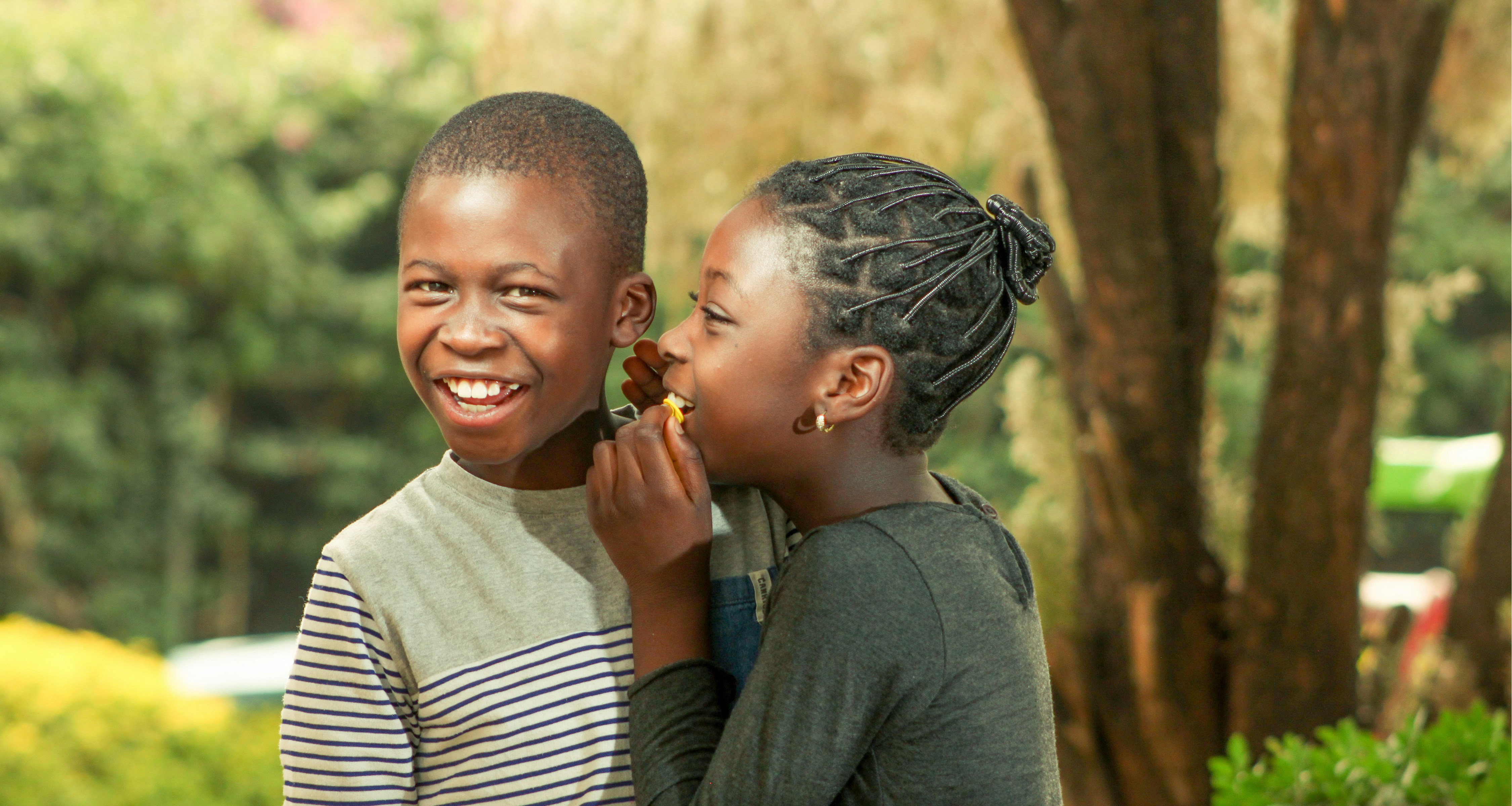 Two children sharing a bite of food, one boy laughing.