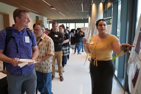 Dr. Fadok and others stand listening to Maria Najjar present in front of her poster