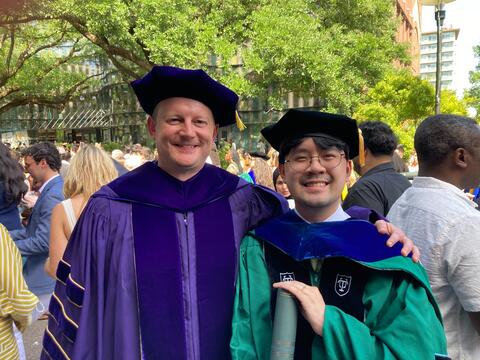 Dr. Le standing next with Dr. Fadok in their commencement attire