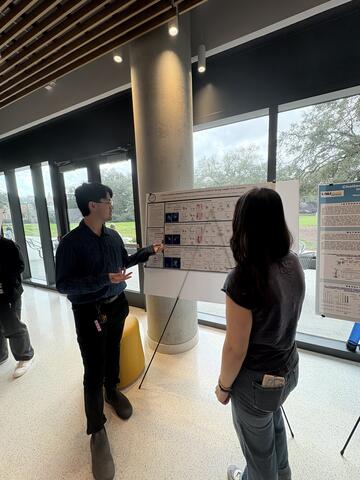 Eric is standing next to his poster presenting to a student.