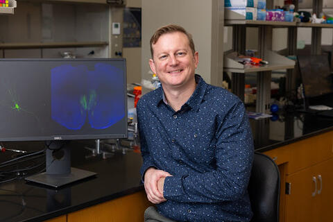 Dr. Fadok sits next to a screen showing IHC staining on a mouse brain slice
