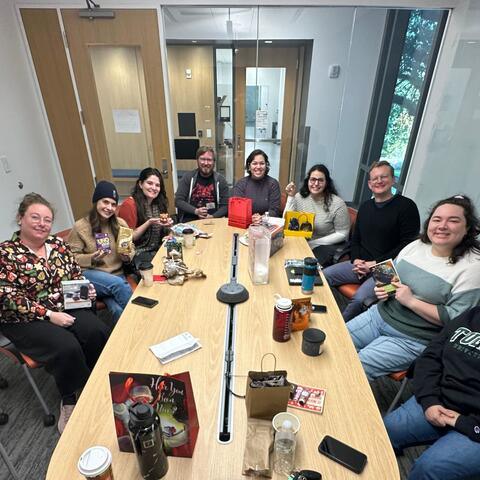 The fadok lab gathered around a table with gifts and wrapping strewn about after having a white elephant secret santa party.