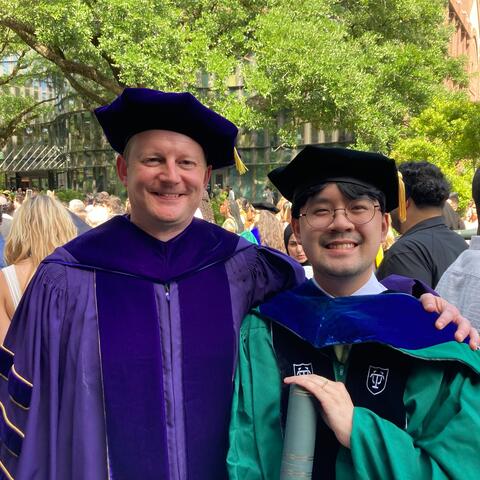 Dr. Le standing next with Dr. Fadok in their commencement attire