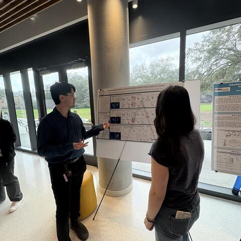 Eric is standing next to his poster presenting to a student.