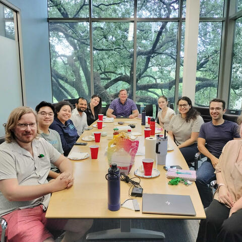 The lab sit around a table eating pizza and celebrating