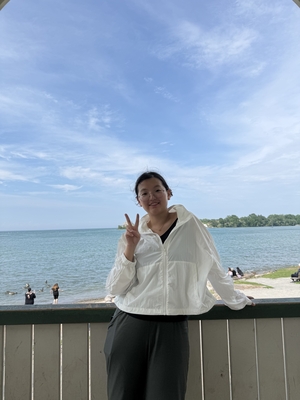 A woman smiling and making a peace sign next to a lake.